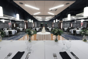 Kalamazoo Room - Event Space - Large room with wooden pillars. Round banquet tables with white linens, chairs surrounding each table, dance floor with wedding cake on a table